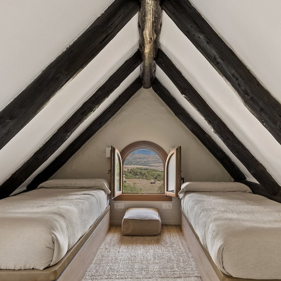 Buhardilla con vigas de madera, dos camas y mini ventana redonda